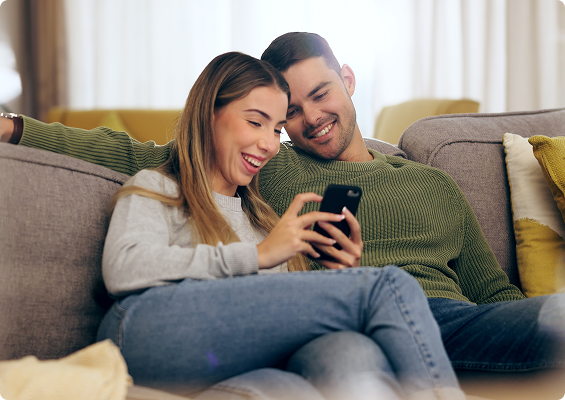 Casal sorrindo no sofá usando celular